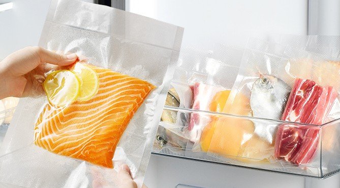 Filete de salmón envasado al vacío con rodajas de limón y otros alimentos almacenados en bolsas selladas dentro de un refrigerador.